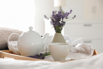 Fototapeta na wymiar Wooden tray with cup of hot tea and beautiful lavender flowers on bed. Tasty breakfast