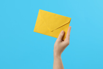 Woman holding yellow paper envelope on light blue background, closeup