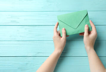 Woman with green paper envelope at light blue wooden table, top view. Space for text