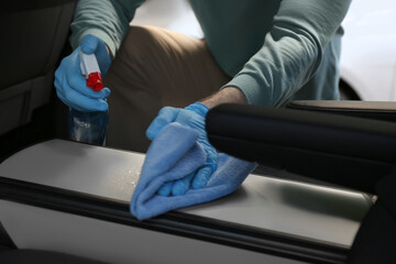 Man in gloves cleaning car with disinfectant spray and rag, closeup. Preventive measure during coronavirus pandemic