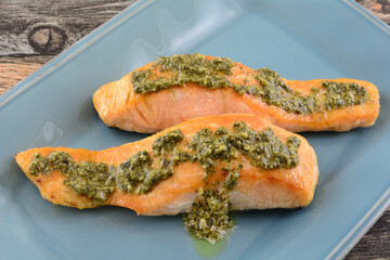 Two baked salmon fish fillets with basil pesto sauce on blue serving platter on table 