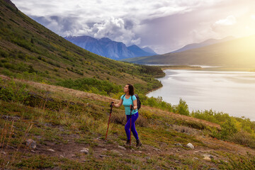 Fototapeta premium Adventurous Girl Hiking up the Nares Mountain during a cloudy and sunny sunset. Taken at Carcross, near Whitehorse, Yukon, Canada.