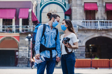 Obraz na płótnie Canvas Tourist couple in a historical latin american city with face mask holding a camera on vacation in coronavirus pandemic