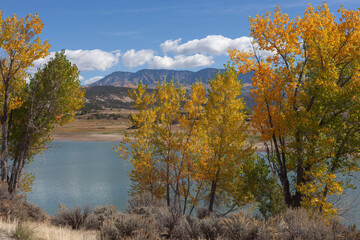 Autumn lake in western Colorado with golden trees in the foreground and mountains in the distance/