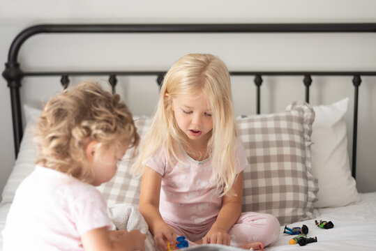 Two little girls in pajamas sitting on the bed playing with toys
