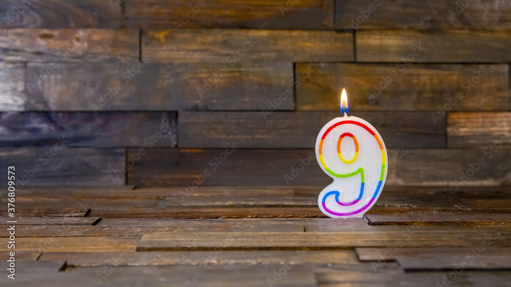 Wall mural Lighted number nine candle on wooden background