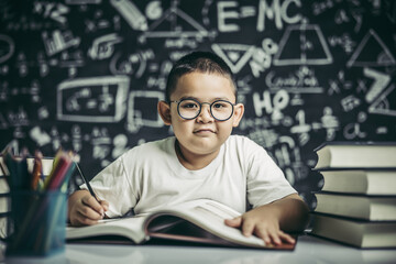 A boy with glasses man writing in the classroom