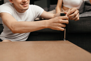 a man in casual clothes repairs a table in his living room with a screwdriver. Family everyday life. close-up plan.