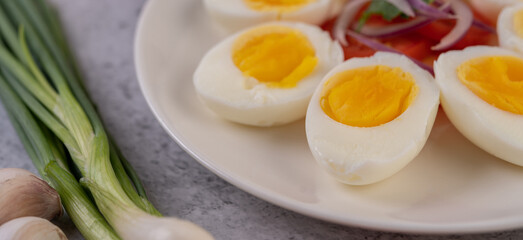 Half boiled egg in a white plate with tomatoes and spring onions.