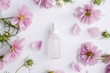 Obraz na płótnie Canvas Glass bottle with pipette next to fresh flowers and petals on white background. Natural beauty product. Flat lay, top view.