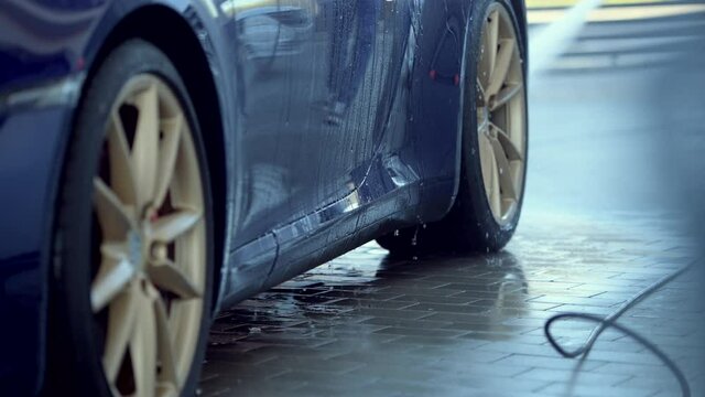 Man Washing Car With High Pressure Water Spray Wand Rinsing Wheels And Rims Of Vehicle With Strong Water Jet. 