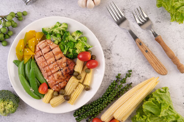 Chicken steak topped with white sesame, peas, tomatoes, broccoli and pumpkin in a white plate.