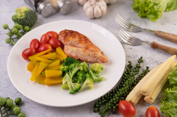 Chicken steak topped with white sesame, peas, tomatoes, broccoli and pumpkin in a white plate.