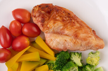 Chicken steak topped with white sesame, peas, tomatoes, broccoli and pumpkin in a white plate.