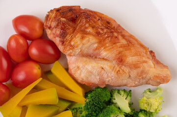 Chicken steak topped with white sesame, peas, tomatoes, broccoli and pumpkin in a white plate.
