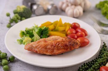 Chicken steak topped with white sesame, peas, tomatoes, broccoli and pumpkin in a white plate.