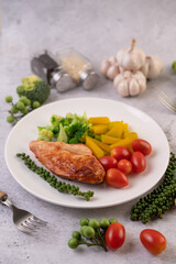 Chicken steak topped with white sesame, peas, tomatoes, broccoli and pumpkin in a white plate.