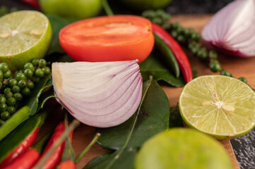 Onion, chili, fresh pepper Kaffir lime leaves and lime placed on a wooden chopping board.