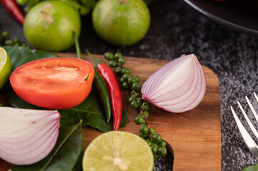 Onion, chili, fresh pepper Kaffir lime leaves and lime placed on a wooden chopping board.