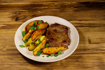 Fried beef steak with potato wedges on wooden table