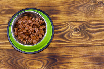 Canned food for cats or dogs in green metal bowl on wooden floor. Top view