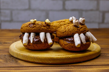 Halloween dessert: Toothed monsters made of oatmeal cookies, chocolate spread and marshmallows on a wooden table