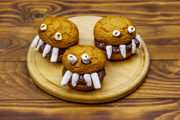 Halloween dessert: Toothed monsters made of oatmeal cookies, chocolate spread and marshmallows on a wooden table