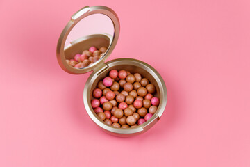 Rouge balls in the open round plastic container with mirror inside lid on a pastel pink background. Top view, flat lay