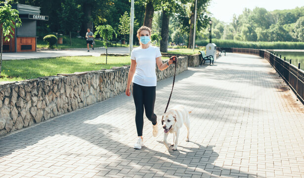 Blonde lady walking outside with medical mask on face with her golden retriever near a lake