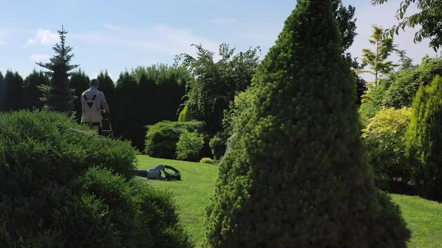 View Of Caucasian Male Gardener Cutting Grass And Taking Care Of Green Lawn In Private Estate During Routine Yard Maintenance. 