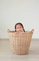 Smiling asian little girl sitting in rattan basket in room at home