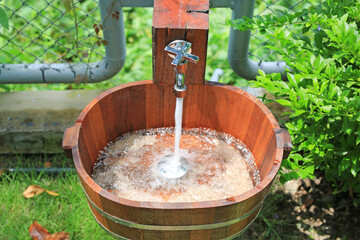 Faucet with water flow into the wooden sink on nature background.