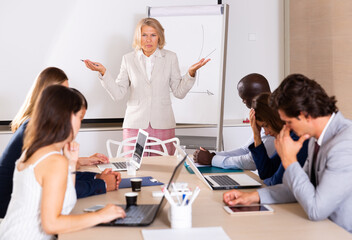 Outraged mature female boss standing near whiteboard in meeting room, expressing dissatisfaction...