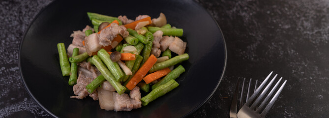 Stir-fried long beans and carrots, add pork belly, put on a black plate.