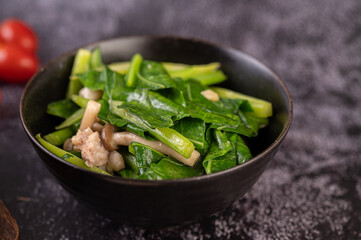 Stir-fried kale and pork belly in a plate placed on a wooden plate.