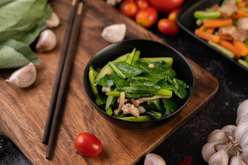 Stir-fried kale and pork belly in a plate placed on a wooden plate.