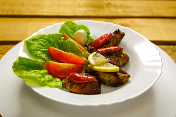 White plate with slices of grilled meat with lemon and tom.