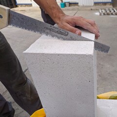 Mason cutting construction blocks made from aerated concrete using handsaw.