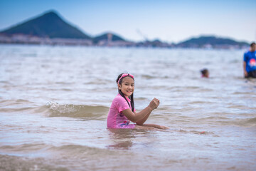Close-up background view of an Asian girl, playing in the sea on the beach, with a parent or guardian supervising during the holidays, family getaways.