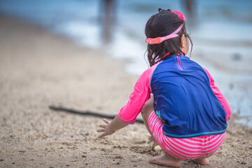 Close-up background view of an Asian girl, playing in the sea on the beach, with a parent or guardian supervising during the holidays, family getaways.
