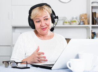Happy mature woman in headphones with microphone communicating via internet
