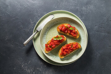 three bruschetta with tomatoes and basil on a plate, vintage knife on a dark background