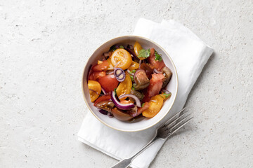 tomato salad in white bowl on white napkin with vintage fork on light concrete background