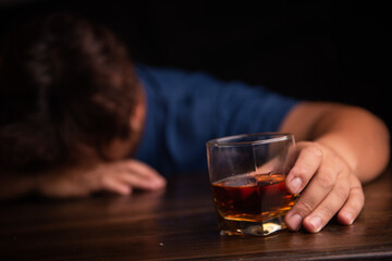 An alcoholic with a glass of whiskey lying on the table at night.