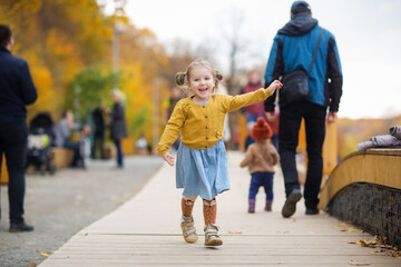 happy child in yellow jacket runs and laughs. child walks in Park in autumn. lots of people in...