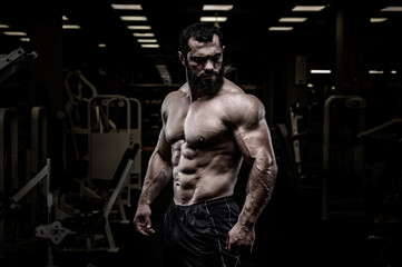 Fototapeta na wymiar handsome healthy young strong bearded caucasian man with perfect sport physique body in dark athlete gym