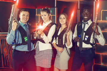 Portrait of smiling males and females in business suits posing at laser tag room