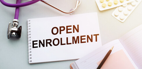 OPEN ENROLLMENT text written in a notebook lying on a medicine desk and a stethoscope. Medical...