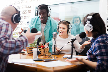 Irritated African male and European female radio presenters emotionally discussing with guests in sound broadcasting station