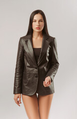 a girl poses in a leather jacket standing with her back against a white background with bare legs